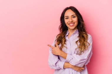 Pembe arka planda izole edilmiş genç Meksikalı kadın işaret parmağıyla işaret ederek gülümsüyor..
