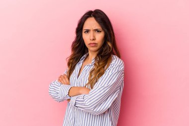 Pembe arka planda izole edilmiş genç Meksikalı kadın hoşnutsuzca kaşlarını çatmış, kollarını kavuşturmuş..