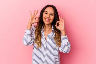 Pembe arka planda izole edilmiş genç Meksikalı kadın neşeli ve kendinden emin..