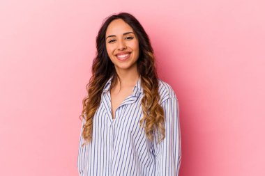 Pembe arka planda izole edilmiş genç Meksikalı kadın ellerini kalçasında tutuyor..