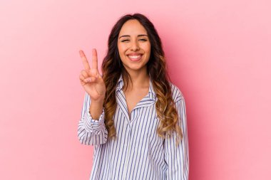 Pembe arka planda izole edilmiş genç Meksikalı kadın iki numarayı parmaklarıyla gösteriyor..