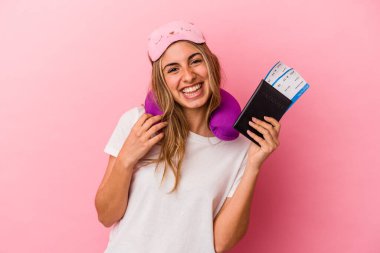 Elinde pasaport ve seyahat biletleri olan beyaz saçlı genç bir kadın pembe arka planda izole edilmiş mutlu, gülümseyen ve neşeli..