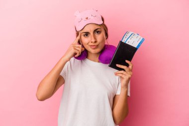Elinde pasaport ve seyahat biletleri olan beyaz saçlı genç bir kadın pembe arka planda izole edilmiş bir şekilde tapınağı parmağıyla göstererek bir göreve odaklanmış..