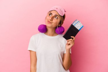 Elinde pasaport ve seyahat biletleri olan beyaz saçlı genç bir kadın pembe arka planda tek başına hedeflerine ve amaçlarına ulaşma hayali kuruyor.