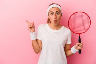 Genç, sarışın, beyaz bir kadın elinde bir badminton raketi tutuyor. Pembe arka planda izole edilmiş.