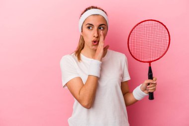 Pembe arka planda izole edilmiş badminton raketi tutan genç sarışın beyaz kadın gizli bir fren haberi veriyor ve yan bakıyor.