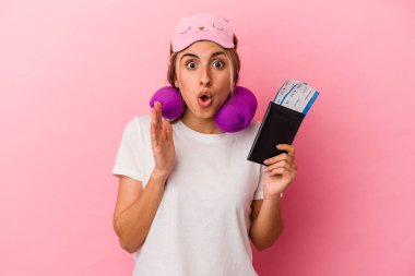 Pasaport ve seyahat biletleri taşıyan beyaz, genç bir kadın. Pembe arka planda tek başına. Şaşırmış ve şok olmuş..