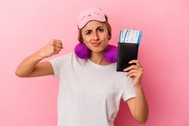 Pasaport ve seyahat biletleri taşıyan beyaz, genç bir kadın pembe arka planda izole edilmiş. Kameraya yumruk, agresif yüz ifadesi gösteriyor..