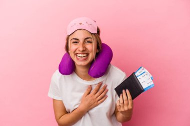 Elinde pasaport ve seyahat biletleri olan beyaz bir kadın pembe arka planda tek başına gülüp eğleniyor..