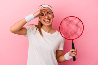Genç, sarışın, beyaz bir kadın elinde badminton raketi tutuyor. Pembe arka planda izole edilmiş. Heyecanlı..