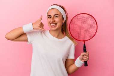 Elinde badminton raketi tutan beyaz bir kadın pembe arka planda cep telefonu hareketini parmaklarıyla gösteriyor..