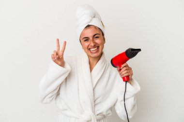 Beyaz tenli, elinde saç kurutma makinesi tutan beyaz bir kadın. İki numarayı parmaklarıyla gösteriyor..