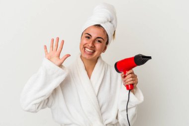 Kafkasyalı genç bir kadın saç kurutma makinesi tutuyor. Beyaz tebessümle 5 numarayı parmaklarıyla gösteriyor..