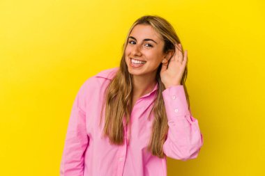Sarı arka planda izole edilmiş genç sarışın beyaz kadın bir dedikoduyu dinlemeye çalışıyor..