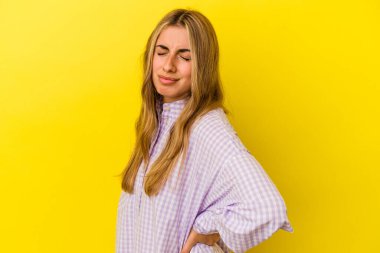 Sarışın, beyaz bir kadın, sarı arka planda izole edilmiş, sırt ağrısı çekiyor..