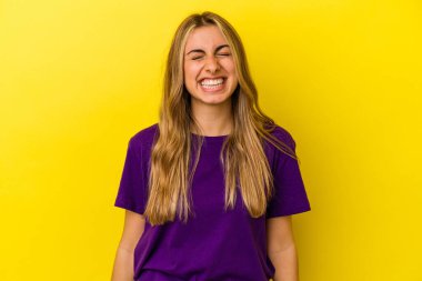 Sarı arka planda izole edilmiş genç sarışın kadın gülüyor ve gözlerini kapıyor, rahatlamış ve mutlu hissediyor..