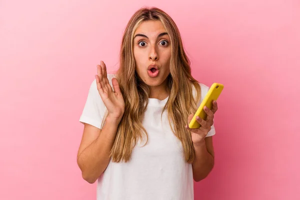 Joven Rubia Caucásica Sosteniendo Teléfono Móvil Amarillo Aislado Sorprendido Sorprendido —  Fotos de Stock