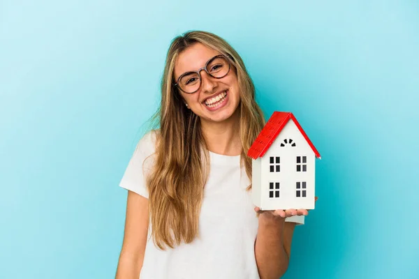 Junge Kaukasische Frau Hält Ein Hausmodell Isoliert Auf Blauem Hintergrund — Stockfoto