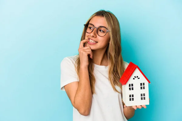 Junge Kaukasische Frau Hält Ein Hausmodell Isoliert Auf Blauem Hintergrund — Stockfoto