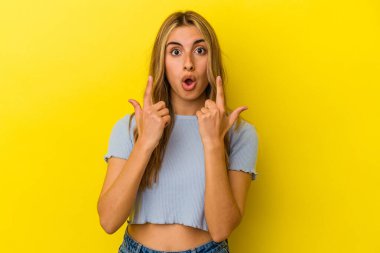 Sarışın, beyaz bir kadın, sarı arka planda izole edilmiş, ağzı açık, üst tarafı işaret ediyor..