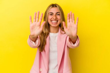 Sarışın, beyaz bir kadın. Sarı arka planda izole edilmiş. Elleriyle on numarayı gösteriyor..