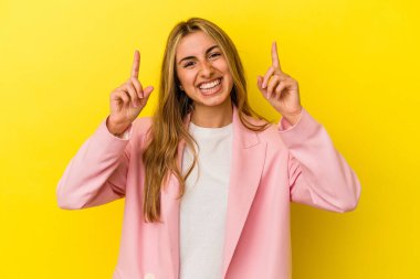 Sarışın, beyaz bir kadın sarı arka planda izole edilmiş. İki parmağı da boş bir alan gösteriyor..