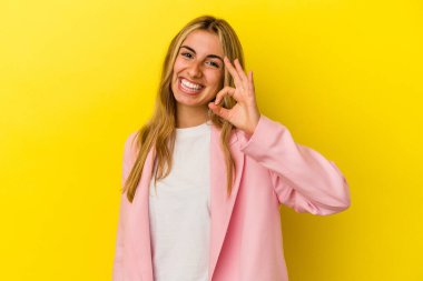 Sarışın, beyaz bir kadın, sarı arka planda izole edilmiş. Göz açıp kapayıncaya kadar elinde iyi bir el hareketi tutuyor..