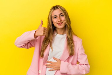Sarı arka planda izole edilmiş genç sarışın kadın karnına dokunuyor, nazikçe gülümsüyor, yemek yiyor ve tatmin oluyor..