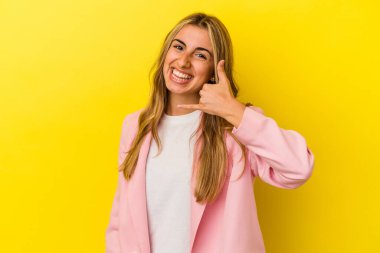 Sarışın, beyaz bir kadın sarı arka planda izole edilmiş. Cep telefonu hareketini parmaklarıyla gösteriyor..