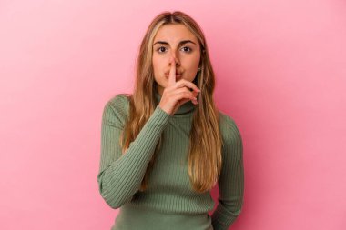 Pembe arka planda izole edilmiş genç sarışın kadın ya sır saklıyor ya da sessizlik istiyor..