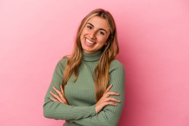 Pembe arka planda izole edilmiş genç sarışın, kendinden emin, kararlılıkla kollarını kavuşturan kadın..