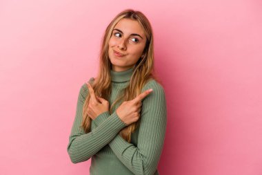 Pembe arka plan noktalarında izole edilmiş genç sarışın beyaz kadın iki seçenek arasından seçim yapmaya çalışıyor..