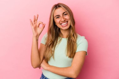 Sarışın, beyaz tenli, pembe arka planda izole bir kadın bir göz kırpıyor ve elleriyle iyi bir jest yapıyor..