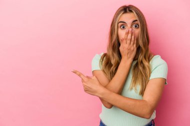 Pembe arka planda izole edilmiş genç sarışın beyaz kadın yan tarafı işaret ediyor.