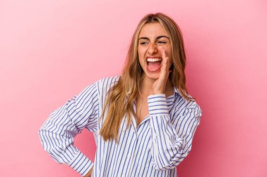 Genç sarışın beyaz kadın pembe arka planda izole edilmiş ve heyecanlı bir şekilde bağırıyor..
