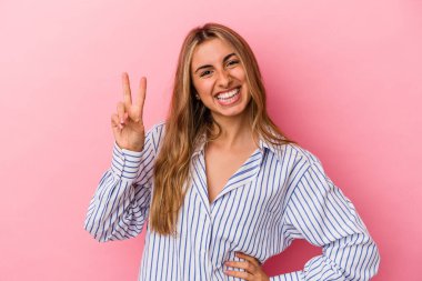 Pembe arka planda izole edilmiş genç sarışın kadın iki numarayı parmaklarıyla gösteriyor..