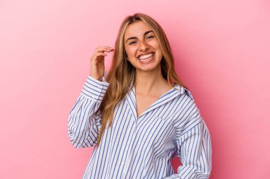 Pembe arka planda izole edilmiş genç sarışın bir kadın bir şeye gülüyor, ağızlarını ellerle kapatıyor..