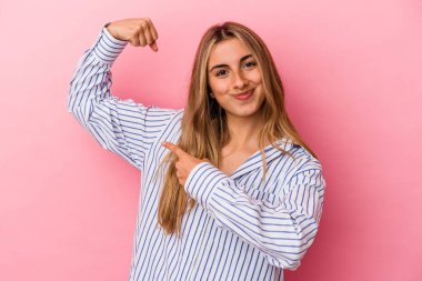 Pembe arka planda izole edilmiş genç sarışın kadın kollarıyla güçlü bir hareket gösteriyor, kadınsı gücün sembolü.