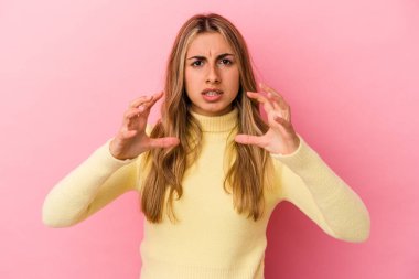 Sarışın, beyaz bir kadın pembe arka planda izole edilmiş. Elinde avuç içi olan bir şeyle kameraya sunuyor..