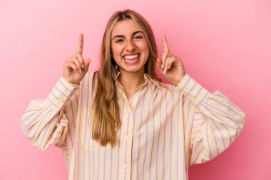 Pembe arka planda izole edilmiş genç sarışın beyaz kadın iki parmağı da boş bir alan gösteriyor..