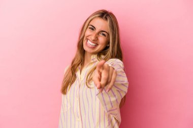 Pembe arka planda izole edilmiş genç sarışın kadın parmaklarıyla ön tarafı işaret ediyor..