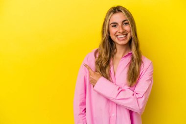 Sarı arka planda izole edilmiş genç sarışın kadın gülümsüyor ve boş alanda bir şeyler gösteriyor..