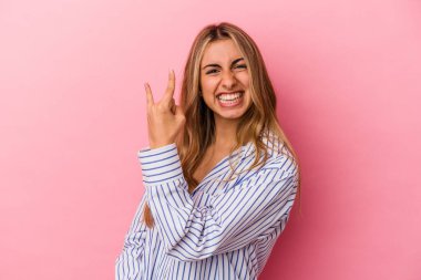 Pembe arka planda izole edilmiş genç sarışın kadın parmaklarıyla taş hareketi gösteriyor.