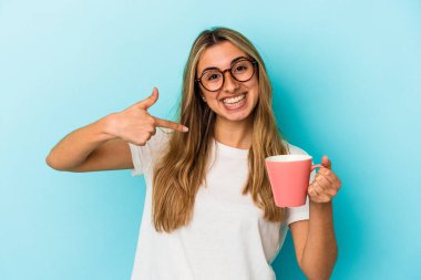 Mavi arka planda bir kupa tutan beyaz, genç bir kadın gömlek fotokopi odasını işaret ediyor, gururlu ve kendinden emin.