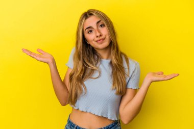 Sarışın, beyaz bir kadın. Sarı arka planda izole edilmiş. Sorgulama sırasında omuz silkiyor ve şüphe duyuyor..