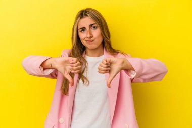 Sarı arka planda izole edilmiş genç sarışın kadın baş parmağını aşağı gösteriyor, hayal kırıklığı konsepti..