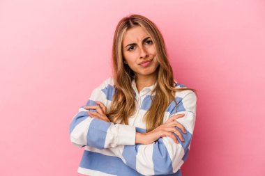 Genç sarışın beyaz kadın pembe arka planda izole edilmiş hoşnutsuzca kaşlarını çatmış, kollarını kavuşturmuş..