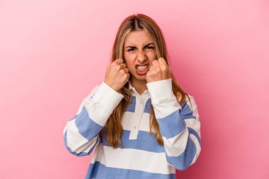 Pembe arka planda izole edilmiş genç sarışın kadın yumruğunu kameraya gösteriyor, agresif yüz ifadesi..