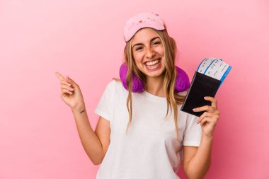 Elinde pasaport ve seyahat biletleri olan beyaz saçlı genç bir kadın pembe arka planda izole edilmiş bir şekilde gülümsüyor ve boş bir alanda bir şey gösteriyor..
