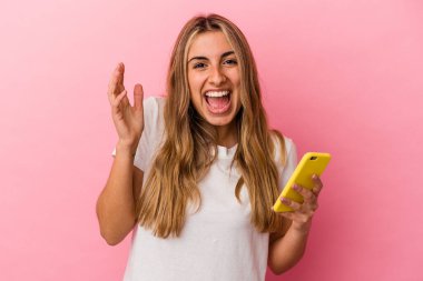 Sarışın, beyaz bir kadın sarı bir cep telefonu tutuyor. Hoş bir sürpriz bekliyor. Heyecanlı ve el kaldırıyor..